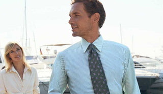Picture of man wearing an Eton shirt and tie at a boat dock, with a woman walking behind him