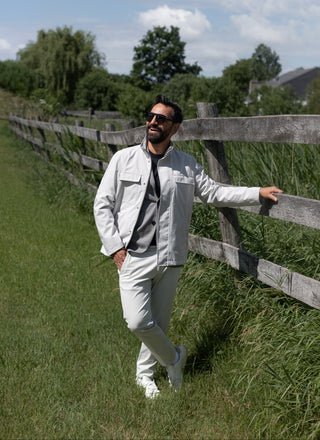 Man in light clothing standing next to a wooden fence with greenery in the background